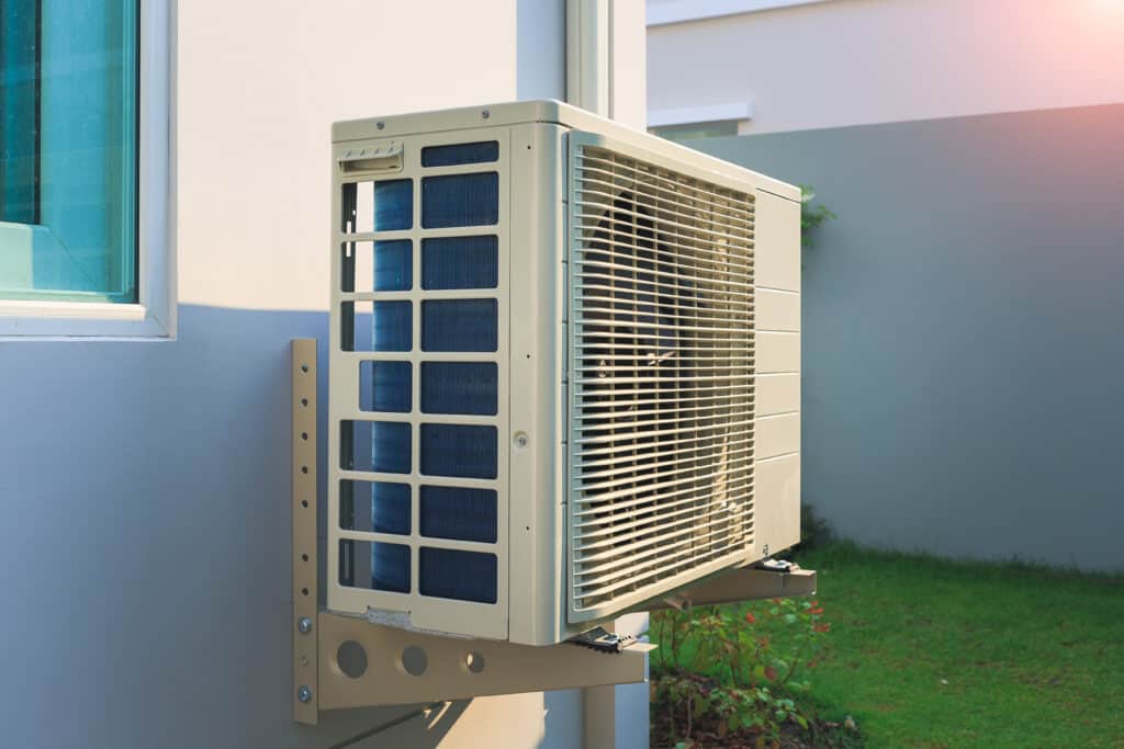Condenser unit or compressor outside home or residential building. Unit of central air conditioner (AC) or heating ventilation air conditioning system (HVAC). Electric fan and refrigerant pump inside.