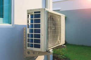 Condenser unit or compressor outside home or residential building. Unit of central air conditioner (AC) or heating ventilation air conditioning system (HVAC). Electric fan and refrigerant pump inside.